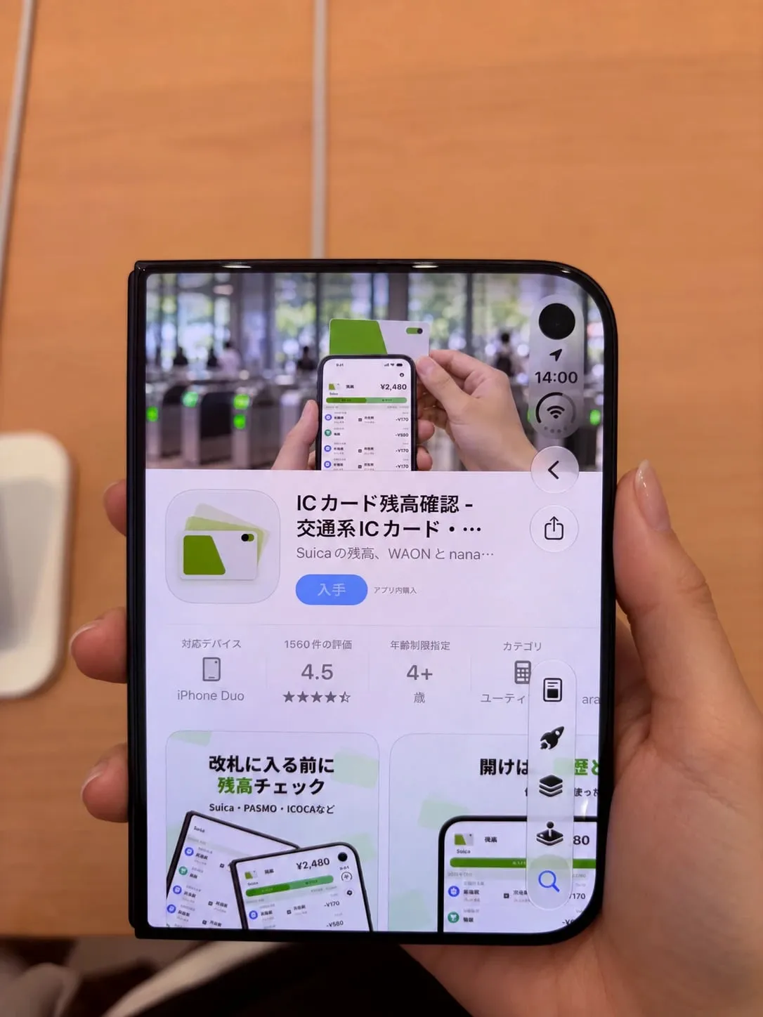 閉じた iPhone Duo を手に持ち、外側の画面に App Store の「ICカード残高確認」のページを表示している。アイコンの下の情報の欄は、左から対応デバイス「iPhone Duo」、評価、年齢制限指定、カテゴリ